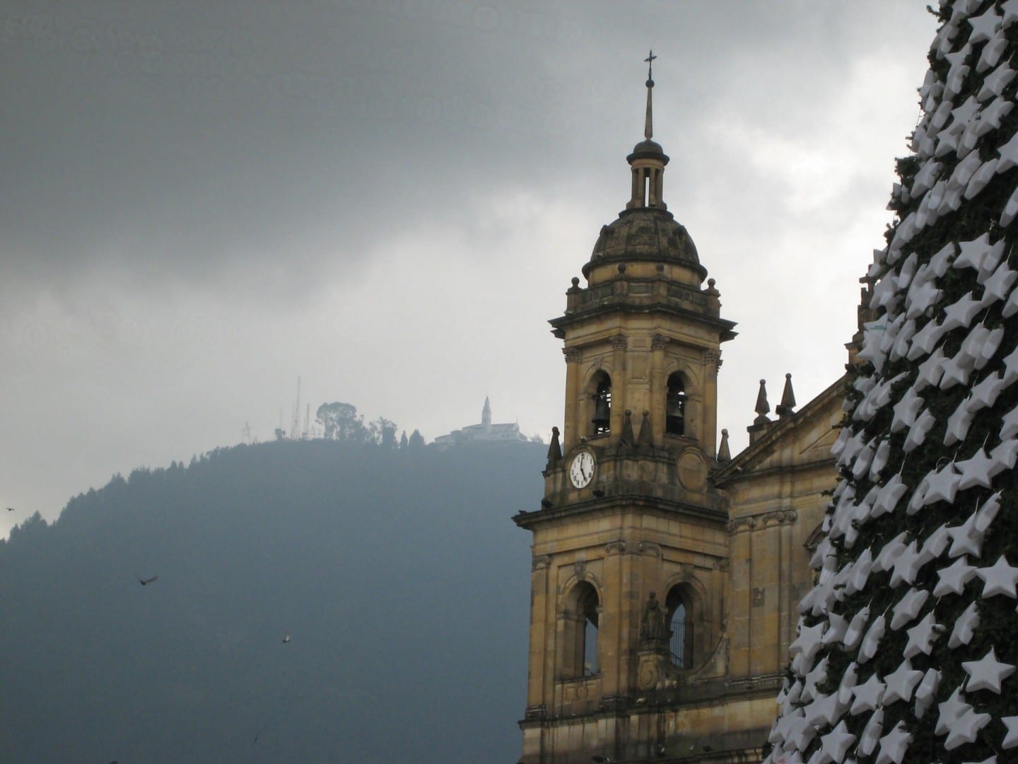 La torre del reloj de la Catedral Primada durante la Navidad, con el Santuario de Monserrate asomándose por encima Bogotá Colombia